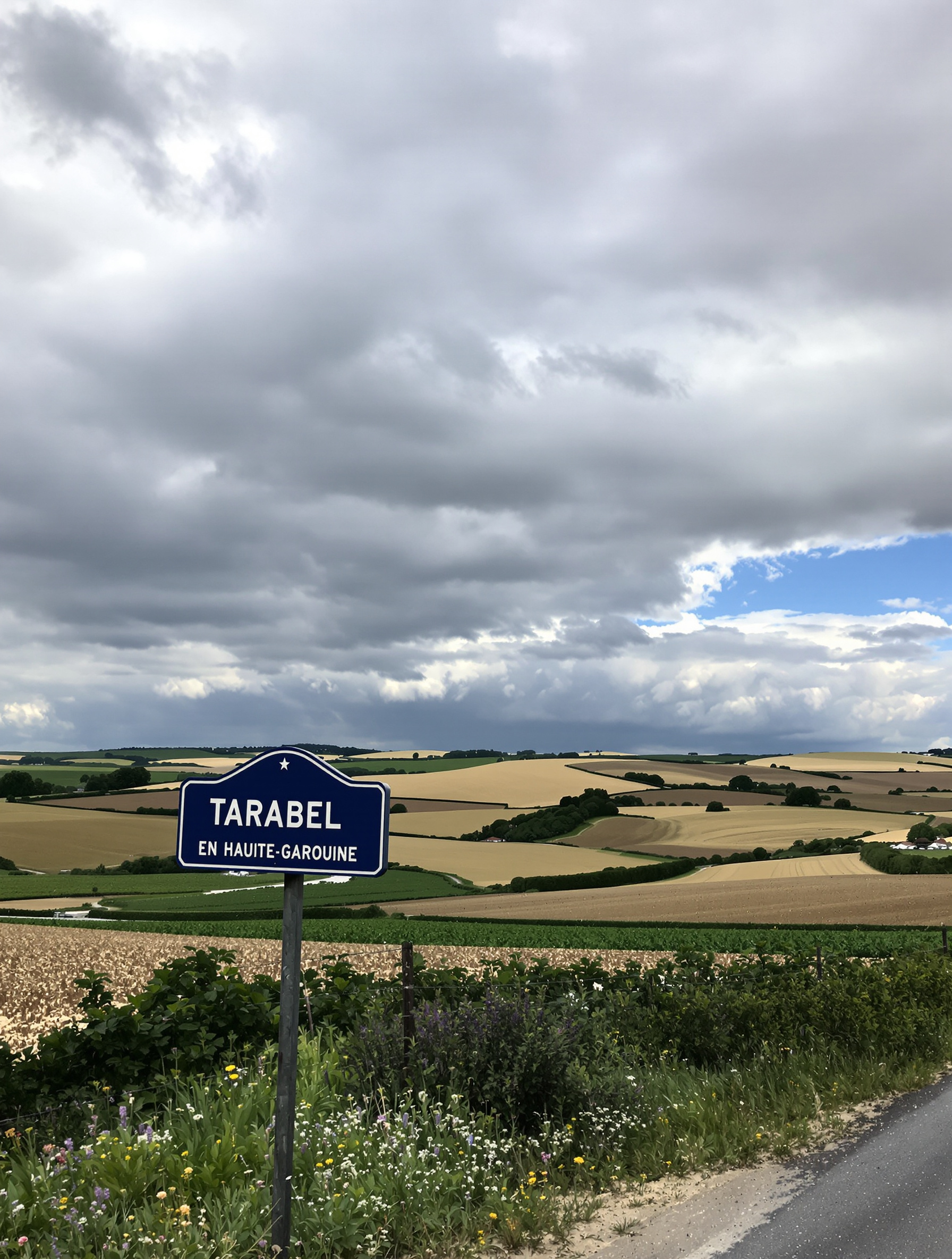 Panneau d'entrée du village de Tarabel avec paysage vallonné typique du Lauragais sous ciel changeant
